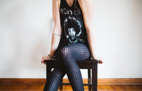 A woman in blue tights and a Bob Marley tank top sits on a stool